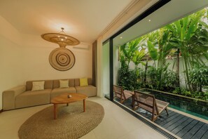 A modern living room with a sofa, coffee table, and a view of a tropical garden through a glass door. - Luxury 2 Bedroom Villa with Private Pool in Umalas (Badung)
