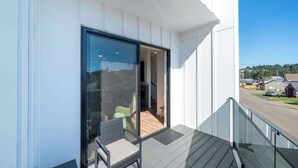 Ein Balkon mit Glastür, einem Korbstuhl und Blick auf eine Straße und Gebäude.