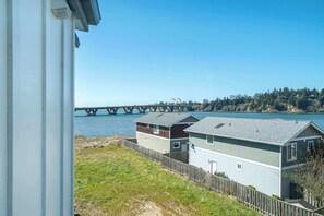 A waterfront property with a view of a bridge, a wooden fence, and a grassy area. - Boho Waldport Retreat + Bay Views, Hot Tub, BBQ (Waldport)