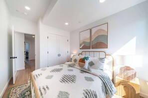 A bedroom with a bed, a nightstand, a lamp, and artwork on the wall. - Boho Waldport Retreat + Bay Views, Hot Tub, BBQ (Waldport)