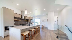 Een moderne keuken met een centraal eiland, houten krukken en een glazen balustrade met uitzicht op een trap.