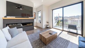 Een moderne woonkamer met een flatscreen-tv, een plafondventilator, een open haard en grote ramen met uitzicht op de stad.