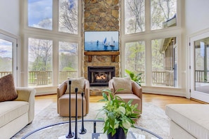 A spacious living room with a stone fireplace, two leather armchairs, a glass coffee table, and a view of the outdoors through large windows. - Majestic Retreat - Game Room Contests, Mountain Views & Movie Nights (Jasper)