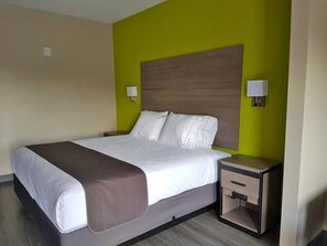 A hotel room with a bed, bedside tables, and a nightstand. - Guesthouse Inn Houston Cypress (Cypress)