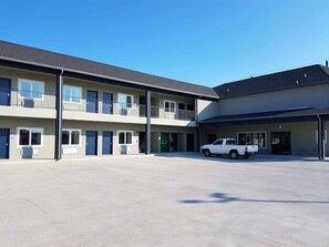A multi-story motel with a covered parking area and a white pickup truck parked in front. - Guesthouse Inn Houston Cypress (Cypress)