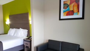 Quarto de hotel com cama, mesa de cabeceira, luminária e um quadro abstrato emoldurado na parede.
