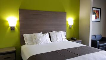 A hotel room with a large bed, two bedside lamps, a nightstand with a phone, and a seating area with a chair.