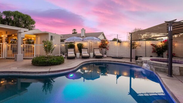 A swimming pool with lounge chairs and umbrellas, a covered patio area, and a building with a white facade. - Swim-In Theater Oasis w/ Gated Pool Sleeps 12 (Indio)