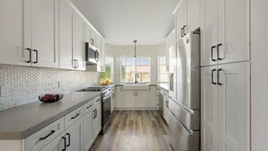 A modern kitchen with white cabinets, a stainless steel refrigerator, and a microwave. - Swim-In Theater Oasis w/ Gated Pool Sleeps 12 (Indio)