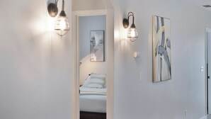 Un couloir avec un lit en arrière-plan, deux appliques murales et deux œuvres d’art encadrées accrochées au mur.
