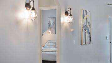A hallway with a bed in the background, two wall-mounted light fixtures, and two framed artworks on the wall.