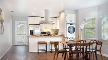 A modern kitchen with white cabinets, a central island, and a dining area with wooden chairs.