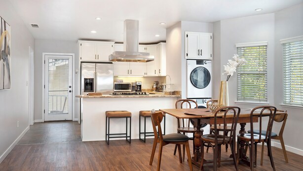 Une cuisine moderne avec des meubles blancs, un îlot central et un coin repas doté de chaises en bois.