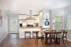 Een moderne keuken met witte kasten, een centraal eiland en een eethoek met houten stoelen.