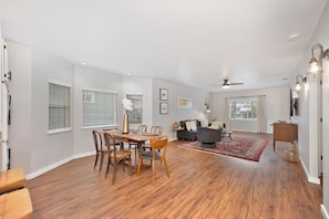 A spacious living room with a dining area, wooden flooring, and a ceiling fan.