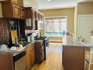 A kitchen with wooden cabinets, a stove, a sink, and a window with blinds.