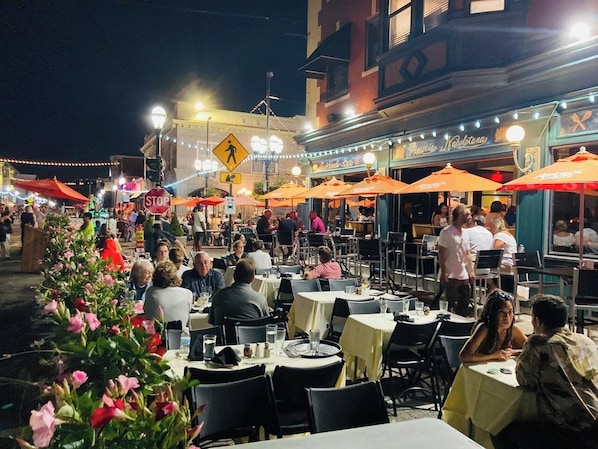 An outdoor dining area with tables and chairs, a pedestrian crossing sign, and a restaurant with outdoor seating.