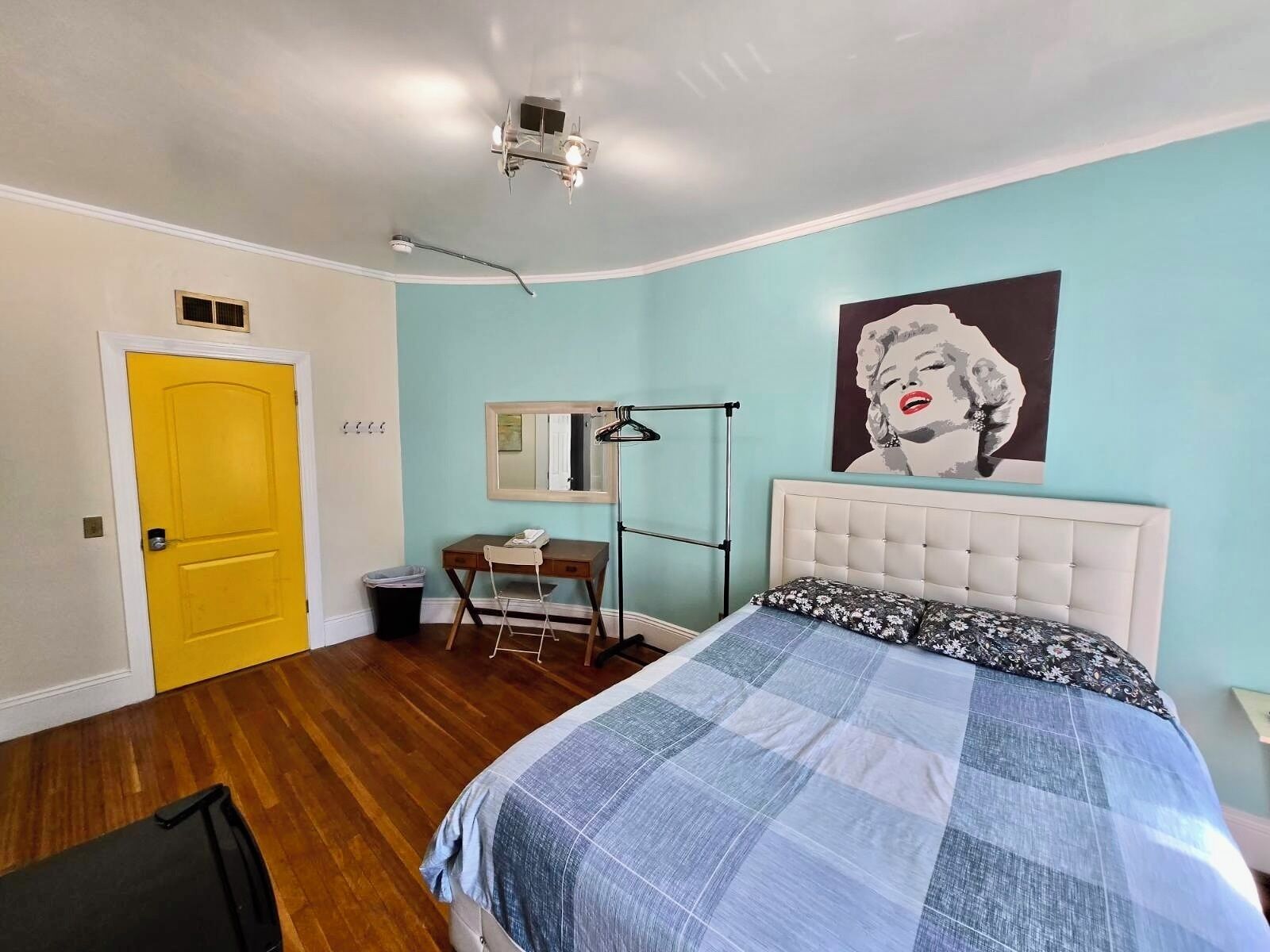 A bedroom with a bed, a desk, a chair, a mirror, and a door.