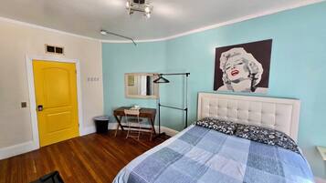 A bedroom with a bed, a desk, a chair, a mirror, and a door.
