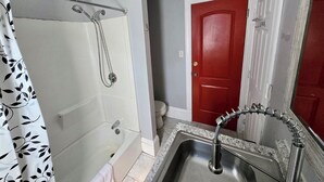 Un bagno con una vasca, una doccia, un lavandino e una porta rossa.