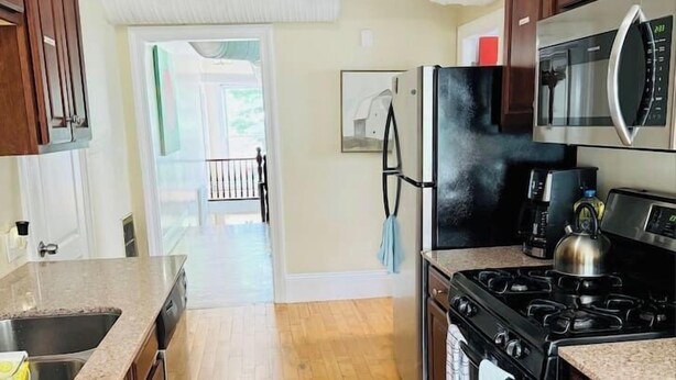 Una cucina con mobili in legno, un frigorifero in acciaio inossidabile, un forno a microonde, un fornello e un lavello.