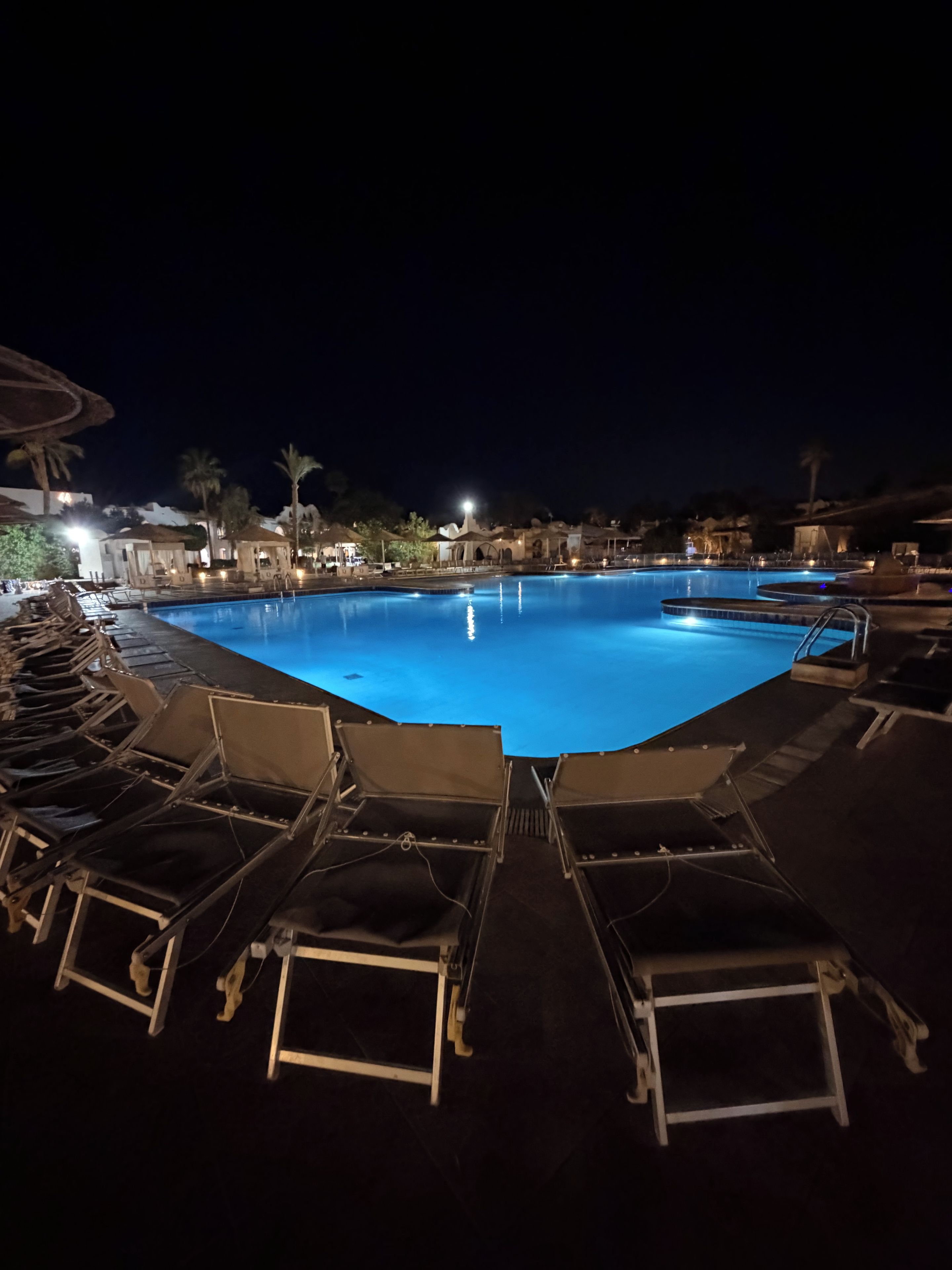 A nighttime swimming pool area with lounge chairs and a clear pool.