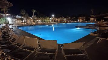 A nighttime swimming pool area with lounge chairs and a clear pool.