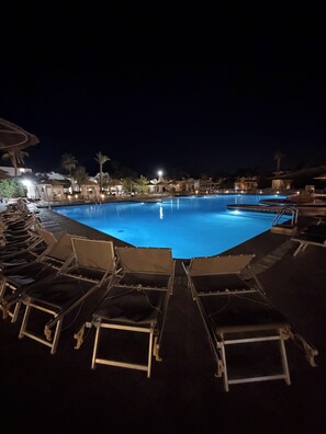 Un espace piscine nocturne avec des chaises longues et une eau cristalline.