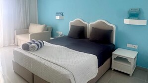 A modern bedroom with a large bed, a bedside table, a nightstand, a chair, and a window with curtains. - MDS Coral Bay Pearl | Sea View | Resort (South Sinai Governorate)