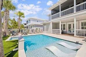 A swimming pool with lounge chairs, a two-story building with balconies, and palm trees.