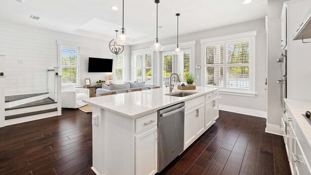 Una cocina moderna con una isla central, muebles blancos e iluminación colgante.