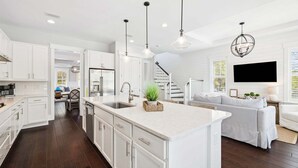 Una cocina moderna con armarios blancos, una isla grande, iluminación colgante y una escalera que lleva a una zona loft.