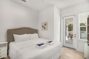 Ein Schlafzimmer mit einem Bett, einem Nachttisch, einer Tür zu einem Außenbereich und einem an der Wand hängenden Kunstwerk.