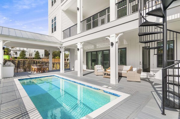 Ein Poolbereich mit überdachter Terrasse, Sitzgelegenheiten im Freien und einer Wendeltreppe.