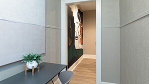 A modern interior with a minimalist design, a wooden table with a potted plant, and a door leading to another room with a large abstract painting. - 2BR Lower Westheimer Dream 01! Walkable to Montrose! (Houston)
