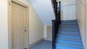 A staircase with blue steps and black railings, a beige door, and a white wall. - 2BR Lower Westheimer Dream 01! Walkable to Montrose! (Houston)