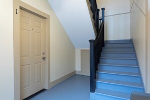 A staircase with blue steps and black railings, a beige door, and a white wall. - 2BR Lower Westheimer Dream 01! Walkable to Montrose! (Houston)