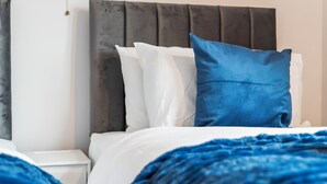 Un letto con cuscini bianchi e azzurri, una testiera grigia e una coperta blu.