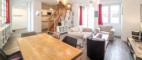 Ein großzügiger Wohnbereich mit einem Holzessttisch, Sofas und einer Treppe, die zur Küche führt.
