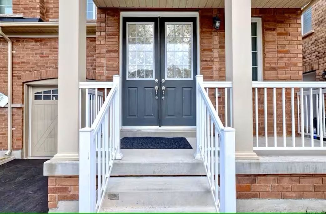 A brick building with a double door, white railings, and a concrete staircase leading to the entrance.