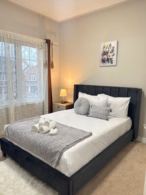 Un lit bien fait, avec des oreillers et une couverture, une lampe de chevet et une œuvre d’art florale encadrée accrochée au mur.