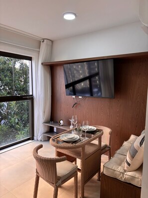 A dining area with a TV mounted on the wall, wicker furniture, and a view through a large window. - Arpoador - On the Sea Copacabana (Rio de Janeiro)