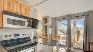 A kitchen with a microwave, stove, and oven, a dining table with chairs, and a view through large windows. - Adventure Trails - Golf View + Hot tub | Waterpark (Wisconsin Dells)