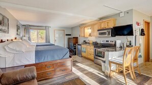 A bedroom with a bed, a desk, and a kitchenette.