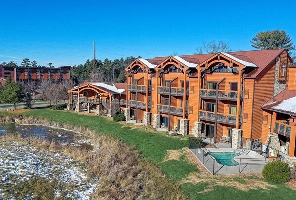 Un chalet à plusieurs étages doté de balcons, d’une piscine et d’un étang.