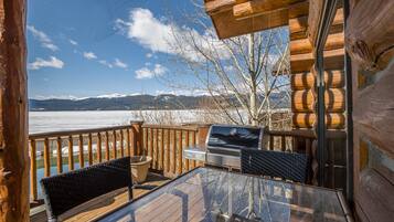 A wooden deck with a grill and chairs, overlooking a body of water and mountains.