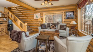 A log cabin interior with a wooden staircase, a sofa set, a coffee table, and a ceiling fan. - Lake house 16 minutes from Yellowstone (West Yellowstone)