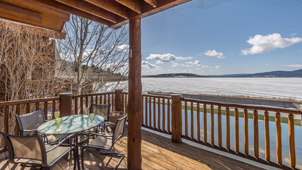 A wooden deck with a table and chairs, overlooking a body of water and distant mountains. - Lake house 16 minutes from Yellowstone (West Yellowstone)