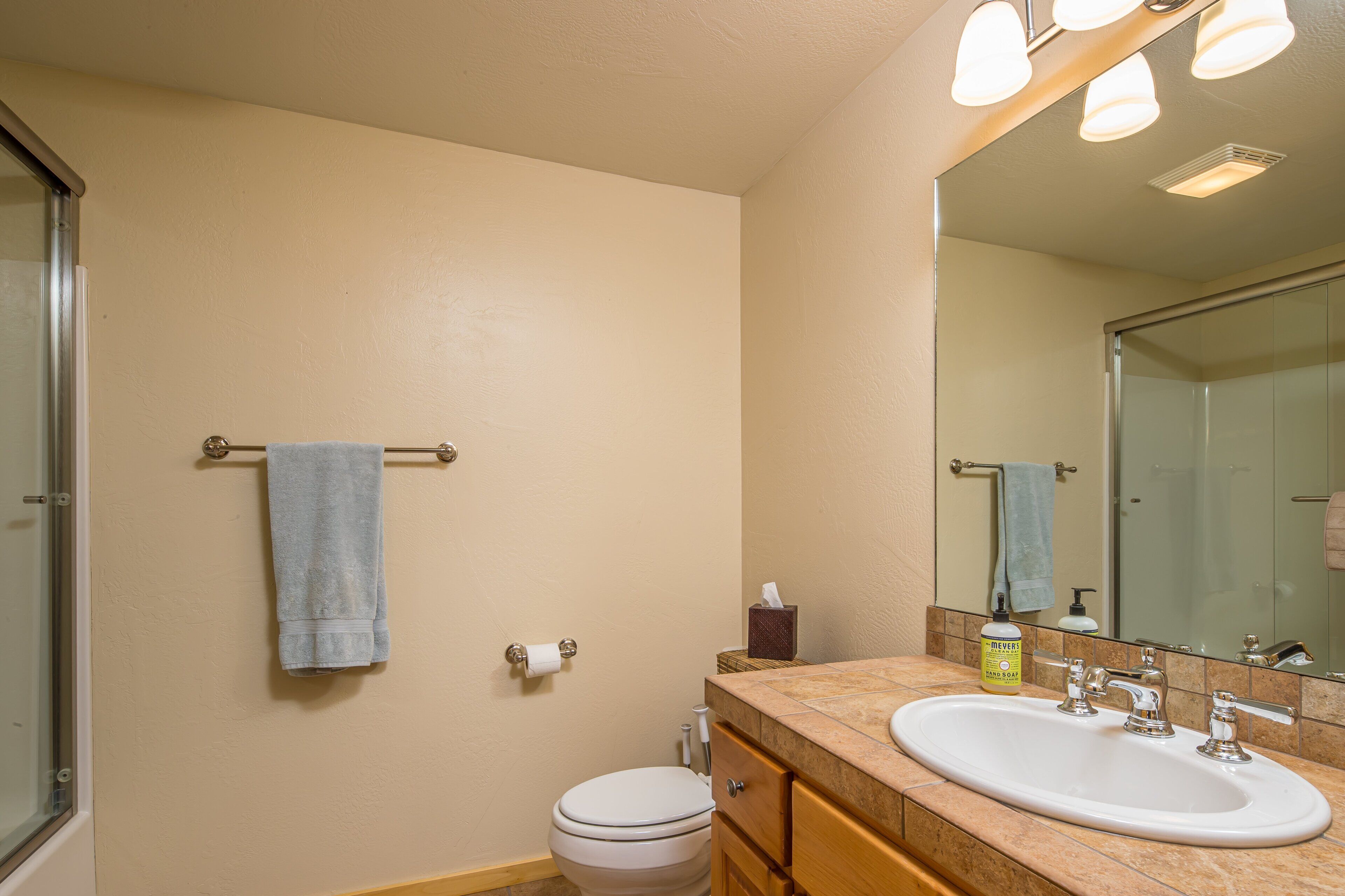 A bathroom with a toilet, sink, mirror, towel rack, and a bottle of hand soap.