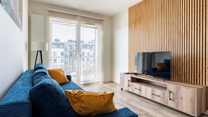 Un salon moderne avec un canapé, un téléviseur, un mur recouvert de panneaux en bois et de grandes fenêtres.